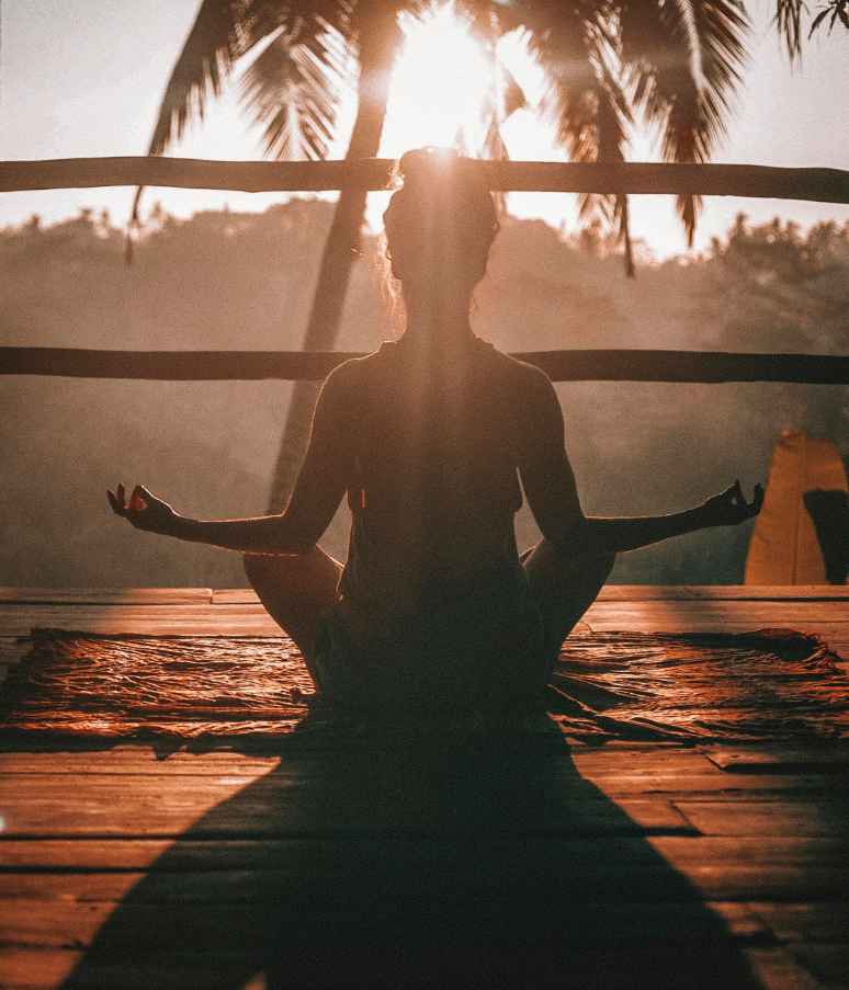 Persona seduta in meditazione al tramonto immersa nella natura per benessere olistico e rilassamento mentale